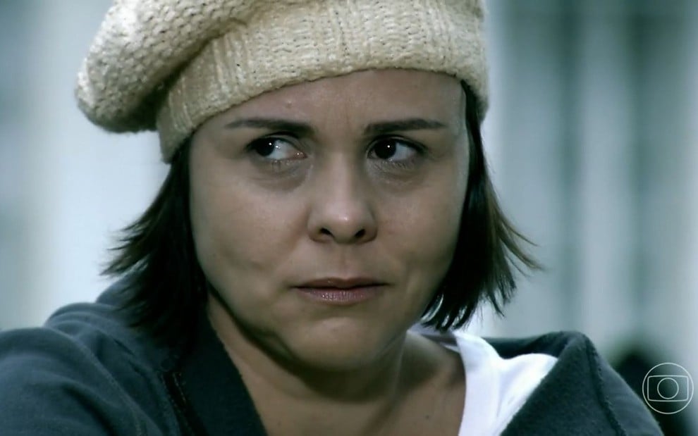 A atriz Giulia Gam como Diva em A Favorita; ela está com um gorro, sentada, olhando para o lado com cara de desconfiada
