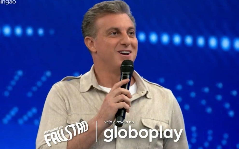 Luciano Huck falando no palco de seu programa na Globo; a tarja está com o nome Domingão do Faustão