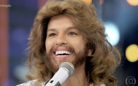 Mariana Rios caracterizada como Barry Gibb na edição do Show dos Famosos, atriz sorri para alguém fora do quadro, está com barba, cabelo volumoso e bigode marrons