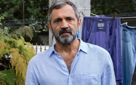 De camisa azul e em frente a varal de roupa, foto Domingos Montagner com expressão séria