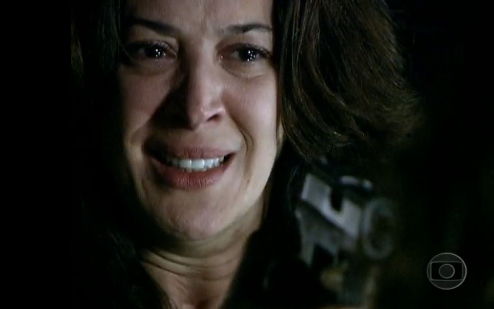 A atriz Claudia Raia como Donatela em A Favorita; ela está segurando uma arma na mão e fazendo cara de choro na novela da Globo