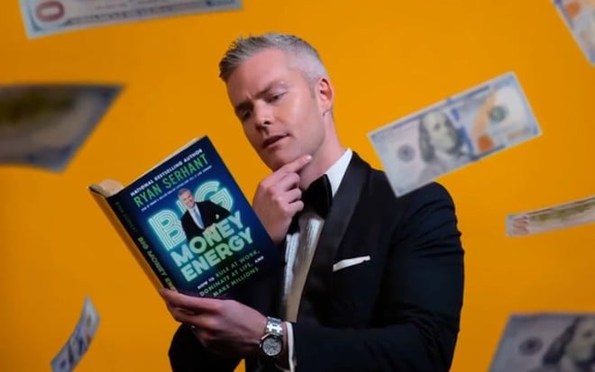 De terno e gravata, Ryan Serhant leva a mão ao queixo enquanto lê seu livro e é cercado por notas de 100 dólares que caem do céu