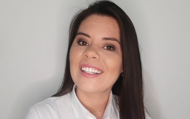 Elaine Trevisan com o uniforme da ESPN e do Fox Sports, com uma camisa branca e a logomarca das duas empresas, em um fundo branco