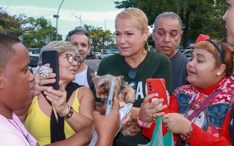 Xuxa junto de alguns fãs; apresentadora aparece com um cachorro no colo e veste camiseta preta