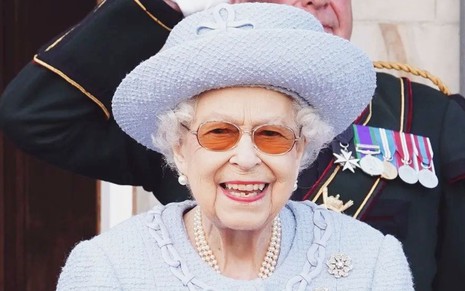 A rainha Elizabeth com um vestido e um chapéu azuis sorri