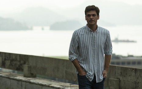 Emilio Dantas, caracterizado como seu personagem em Sob Pressão, está com uma blusa listrada de mangas compridas