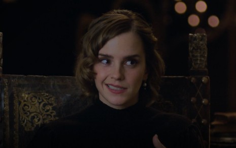 Emma Watson durante entrevista para o especial de 20 anos de Harry Potter. Ela está sentada e com uma blusa preta de gola alta fazendo um semblante de deboche.