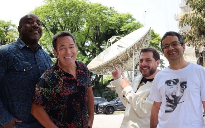 Angelo Campos (à esq.), Tatola Godas, Dennys Motta e Ricardinho Mendonça sorridentes em foto com antena da Band ao fundo