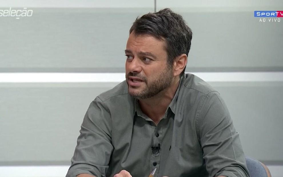 Eric Faria no Seleção SporTV com uma camisa cinza e debatendo assuntos com André Rizek