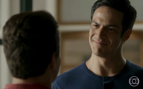 Eric (Mateus Solano) sorri e olha para Júlio (Thiago Martins), que está de costas, em cena da novela Pega Pega