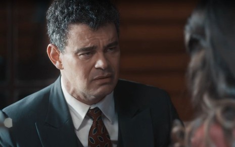 Em cena de Amor Perfeito, Carmo Dalla Vecchia usa terno e gravata e fala com Camila Queiroz, que está de costas
