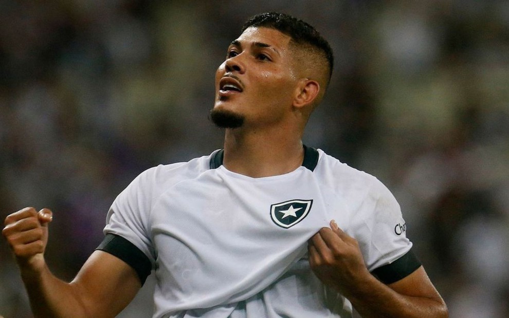 Erison, do Botafogo, comemora gol e puxa escudo com a mão de uniforme branco com detalhes pretos