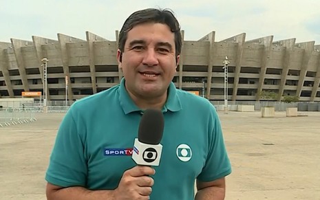 Eudes Junior na porta de estádio em cobertura esportiva; ele usa uniforme verde da Globo e segura microfone