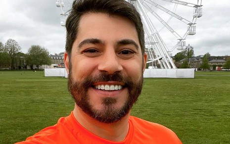 Evaristo sorri, veste camiseta laranja e está na frente de um gramado