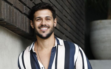 Ex-BBB Rodrigo Mussi usa camisa com listra azul e branco e sorri em pose para foto