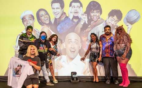 Imagem do elenco do Vai que Cola na frente de um telão com a imagem de Paulo Gustavo