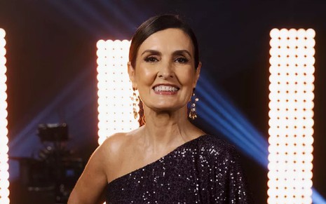 Fátima Bernades com um sorriso, usando uma blusa preta em uma chamada da Globo