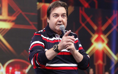 O apresentador Fausto Silva no Domingão do Faustão, com microfone numa mão e dedo em riste em outra