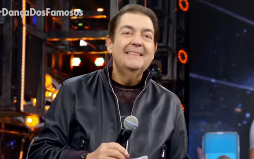 Fausto Silva sorrindo, segurando um microfone, e usando uma jaqueta de couro
