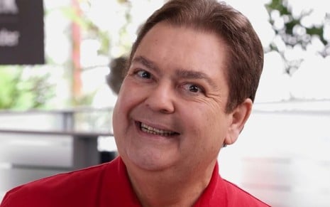 Fausto Silva usa camisa polo vermelha e sorri para a câmera em ação comercial para um banco