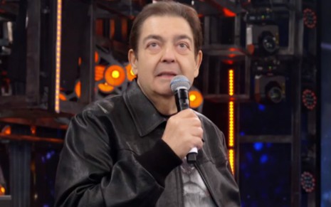 Fausto Silva segura o microfone no cenário do Domingão do Faustão (1989-2021)
