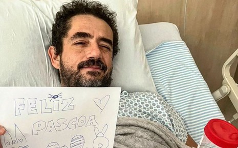 Felipe Andreoli no leito de um hospital segura uma placa em que se lê 'feliz páscoa'