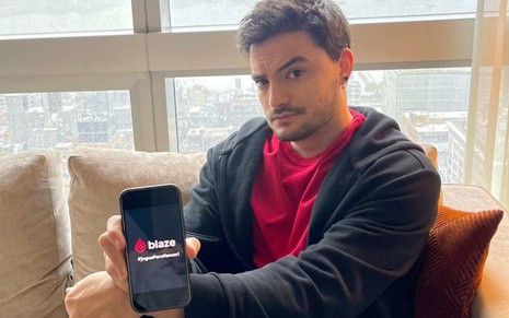 Felipe Neto sentado em um sofá segurando um celular com o logo da Blaze