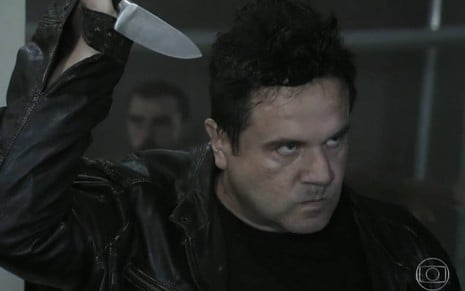 Ator Laércio Fonseca levanta o braço, segura faca, e faz cara de nervoso em cena da novela Império