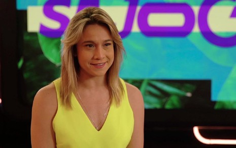 Fernanda Gentil usa uma camisa amarela e está falando com a câmera. Ela está sentada e usa também um batom vermelho no cenário do Se Joga em 2019.