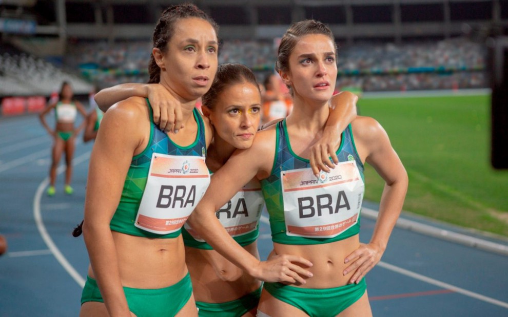 Adriana (Thalita Carauta), Maria Lúcia (Fernanda Freitas) e Sofia (Priscila Steinman) de uniforme de atletismo na pista olhando para o lado direito em cena do filme 4x100 - Correndo Por um Sonho
