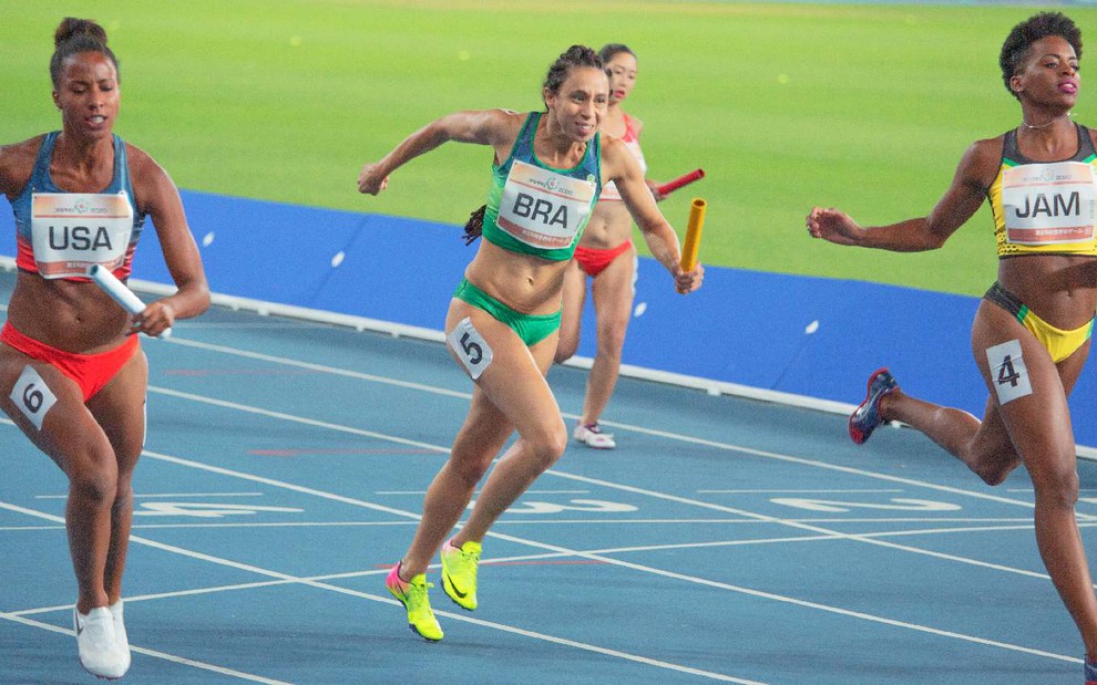 Adriana (Thalita Carauta) em corrida de atletismo com uniforme do Brasil e com um bastão na mão esquerda em cena do filme 4x100 - Correndo Por um Sonho