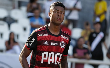 Bruno Henrique, do Flamengo, caminha em campo e veste uniforme listrado em preto e vermelho