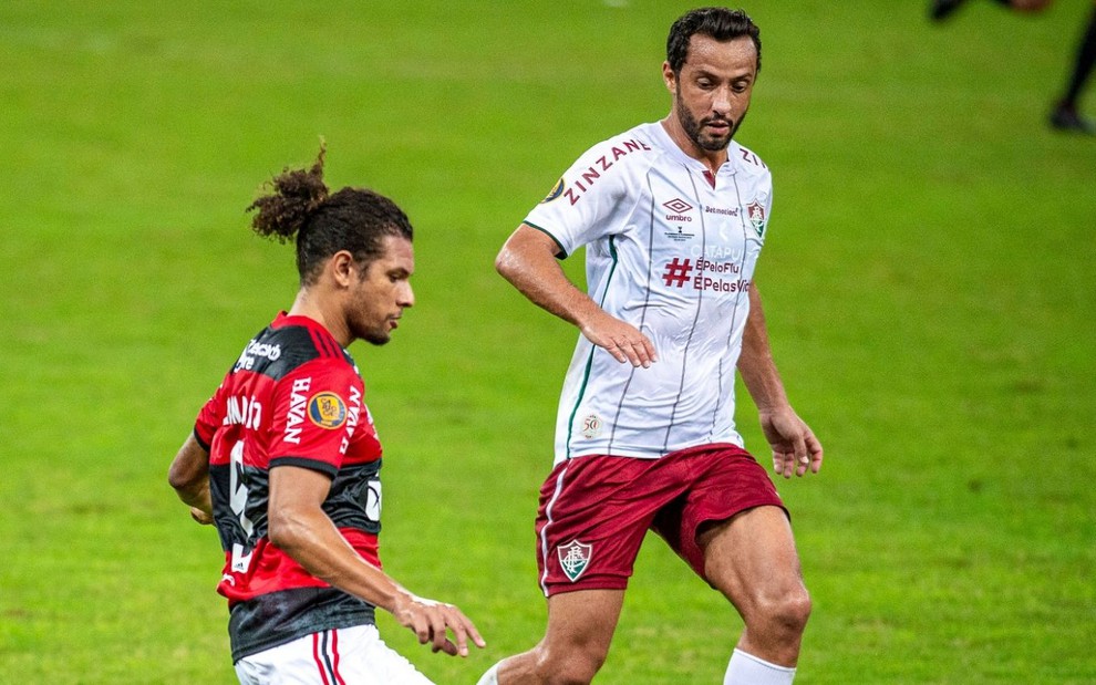 O jogador do Flamengo Willian Arão corre para chutar a bola, enquanto é marcado por Nenê, do Fluminense