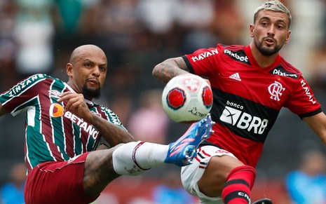 Felipe Melo (do Fluminense) e Arrascaeta (do Flamengo) estão disputando a bola em jogo do Campeonato Carioca