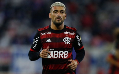 Jogador Arrascaeta, do Flamengo, caminha em campo e veste uniforme listrado em vermelho e preto