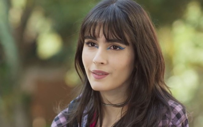 Valentina Herszage usa camisa xadrez e está com cabelos soltos em cena como Flávia na novela Quanto Mais Vida, Melhor!