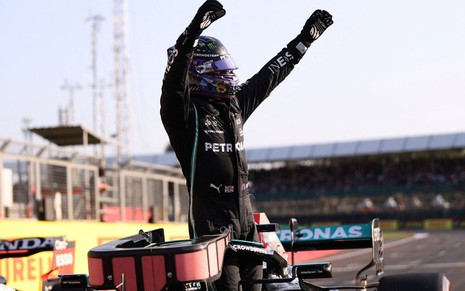 Com o braços erguidos, Lewis Hamilton se levanta no carro e vibra enquanto olha para a torcida