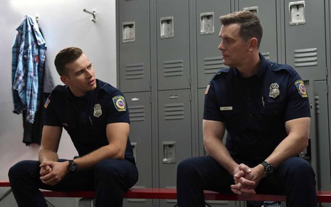 Oliver Stark e Peter Krause se encaram cabisbaixos em um vestiário policial em cena da série 9-1-1
