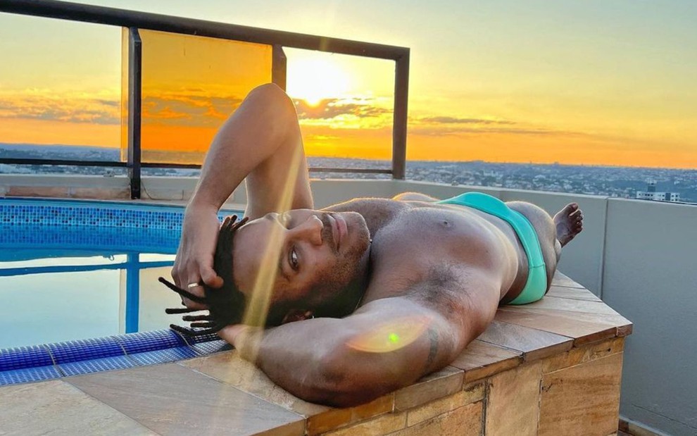 Fred Nicácio deitado de sunga à beira de uma piscina durante o pôr do sol