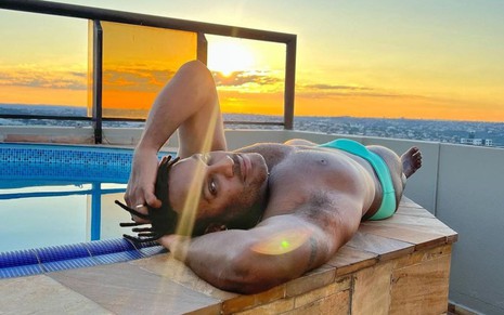 Fred Nicácio deitado de sunga à beira de uma piscina durante o pôr do sol
