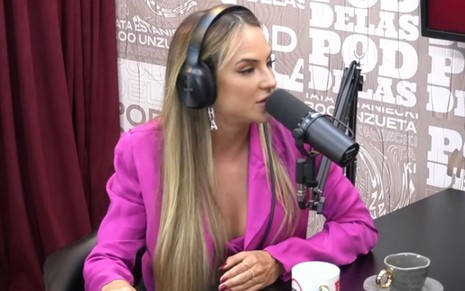 Gabi Martins em entrevista no podcast Poddelas; ela veste um terno rosa, está sentada de fones de ouvido e próxima a um microfone