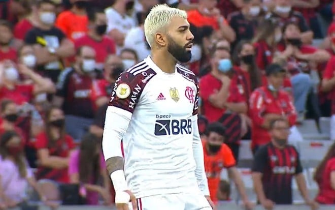 Gabigol com o uniforme branco do Flamengo durante jogo contra o Athletico-PR; a torcida do Furacão está ao fundo