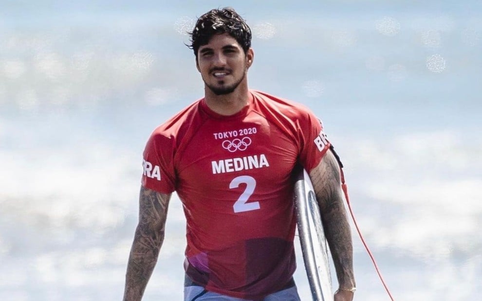 Gabriel Medina sai do mar, usa roupa vermelha e segura uma prancha durante os Jogos Olímpicos de Tóquio