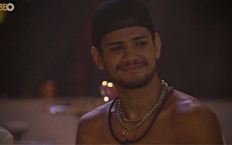 Gabriel Santana sem camisa na festa do BBB 23; ele olha para o lado e usa um boné