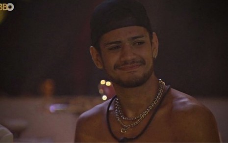 Gabriel Santana sem camisa na festa do BBB 23; ele olha para o lado e usa um boné