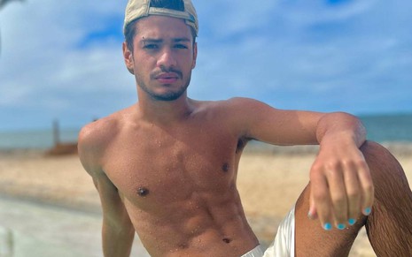 Gabriel Santana sentado em frente a uma piscina e de costas para a praia