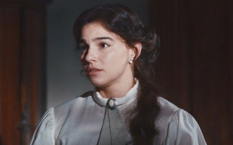 Gabriela Medvedovski está com expressão séria e veste uniforme de médica em cena como Pilar na novela Nos Tempos do Imperador
