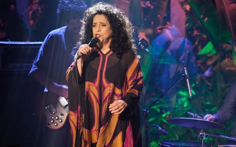 A cantora Gal Costa durante uma cena de Babilônia; ela está em cima do palco, segurando um microfone e cantando