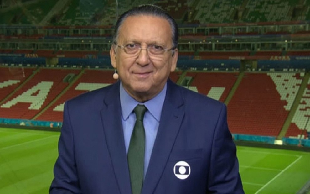Galvão Bueno com uma blusa azul e calça marrom, no estúdio da Globo na Copa da Rússia de 2018