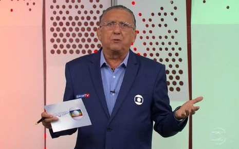 Galvão Bueno nos estúdios da Globo no Rio de Janeiro, com camisa e terno azul, apresentando uma transmissão de futebol na Globo
